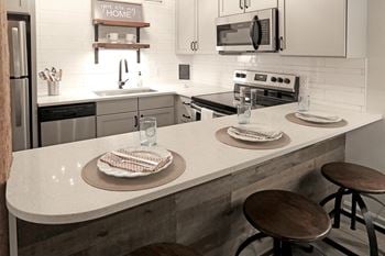 Kitchen island with glassware and plates in front of each barstool, kitchen in background
